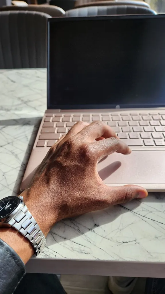 Hand on laptop at a marble cafe table in sunlight